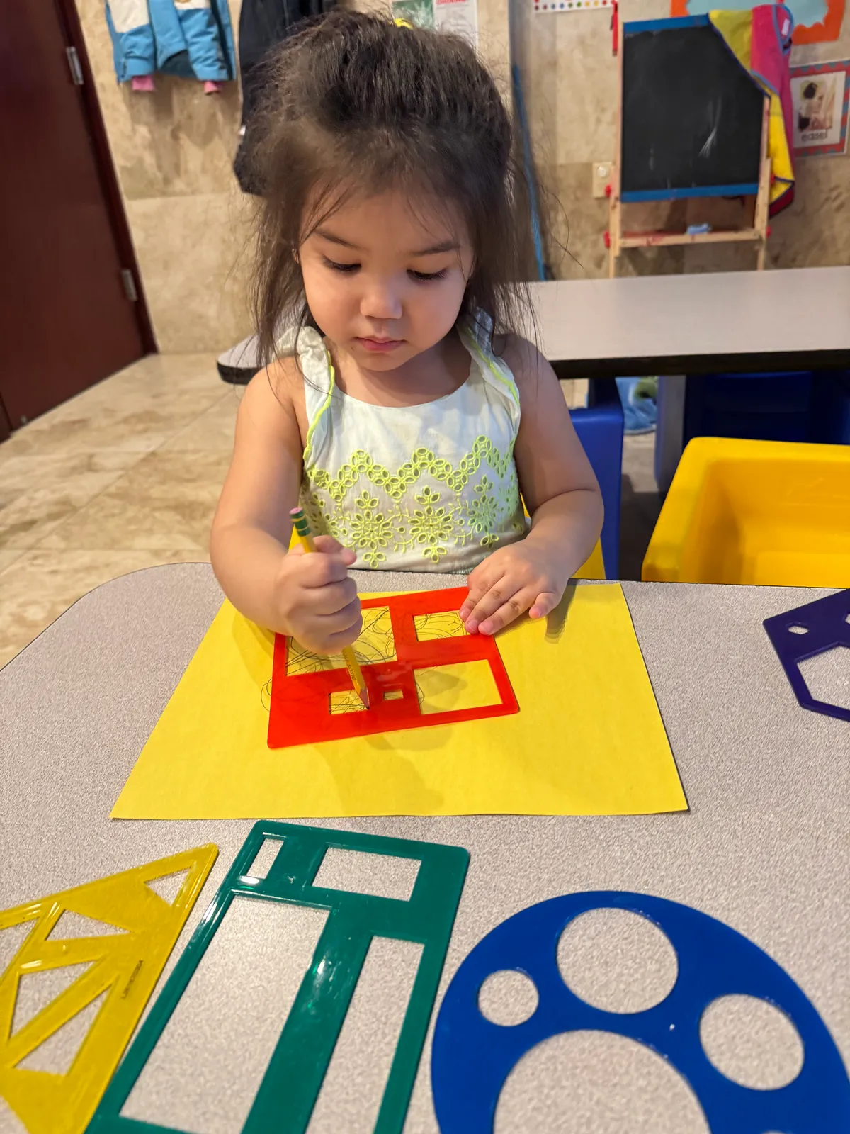 A child tracing shapes onto yellow paper with a pencil